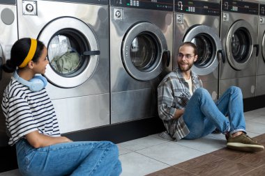Çamaşırhanedeki çift otomatik çamaşır makinesinin çamaşır işlerini bitirmesini beklerken konuşuyor.