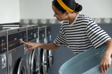 Çamaşır makinesini kullanan bir kadın açmak için düğmeye basıyor.