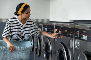 Çamaşırhanede çalışan yetişkin bir kadın ev işlerini tamamlamak için bozuk para makinesi kullanıyor.