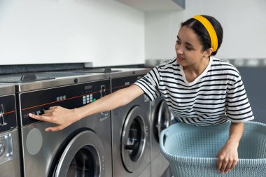 Çamaşırhanedeki kadın, modern çamaşırhanedeki kirli çamaşırları yıkamak için self servis çamaşır makinesi kullanıyor.
