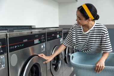 Çamaşırhanedeki kadın, modern çamaşırhanedeki kirli çamaşırları yıkamak için self servis çamaşır makinesi kullanıyor.