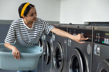 Çamaşır makinesini kullanan bir kadın açmak için düğmeye basıyor.