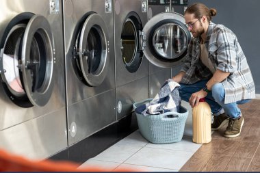 Çamaşırhanede çalışan yetişkin bir adam ev işlerini tamamlamak için bozuk para makinesi kullanıyor.