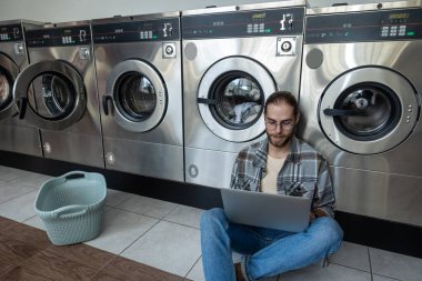 Çamaşırhanede çalışan bir adam temiz kıyafetler beklerken kablosuz internet kullanıyor.