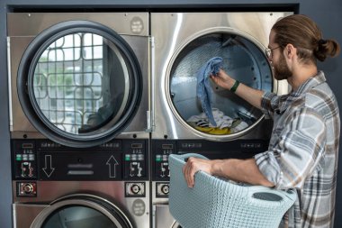 Çamaşırhanedeki sakallı adam kirli çamaşırları çamaşır makinesine yüklüyor.