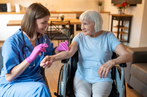 Yaşlı bir hastaya şırınga enjekte ederek hastalığa karşı koruma sağlayan tıbbi pratisyen.