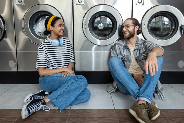 Çamaşırhanedeki çift otomatik çamaşır makinesinin çamaşır işlerini bitirmesini beklerken konuşuyor.