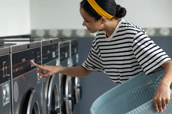 Çamaşır makinesini kullanan bir kadın açmak için düğmeye basıyor.