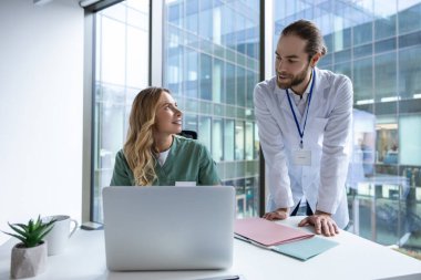 Hastane ofisindeki kadın doktor dizüstü bilgisayarda çalışıyor meslektaşıyla tıbbi araştırmaları tartışıyor.