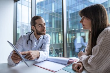 Hastanedeki cerrah masada dijital tablet kullanarak hastayla sağlık prosedürlerini tartışıyor.