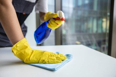 Dezenfekte. Temizlik ekibinden bir kadın masa yüzeyini dezenfekte ediyor.