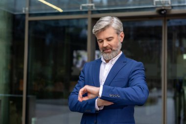 Randevu. Sakallı beyaz iş adamı birini beklerken saatine bakıyor.