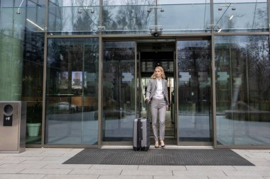 İş gezisi. Güzel takım elbiseli zarif sarışın kadın bir bavul taşıyor.