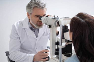 Erkek uzman modern ekipmanlarla göz hekimliği kliniğinde kadın görüşünü kontrol ediyor.