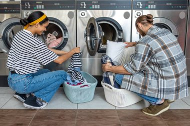 Çamaşırhanede kocası olan bir kadın kirli çamaşırları ev işleri için bozuk para ile çalışan çamaşır makinesine yüklüyor.