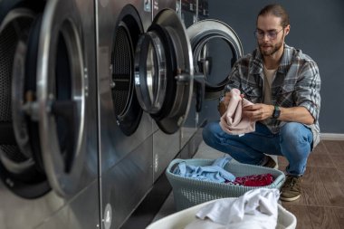 Çamaşırhanede elinde yeni yıkanmış giysiler tutan bir adam var.