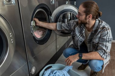 Kamu odasındaki çamaşır ve kurutma makinesini kullanarak self servis ticari çamaşırhanesinde çalışan pozitif bir adam.
