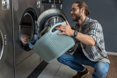 Çamaşırhanedeki adam yıkadıktan sonra temiz çamaşırları kurutucuya koyuyor.