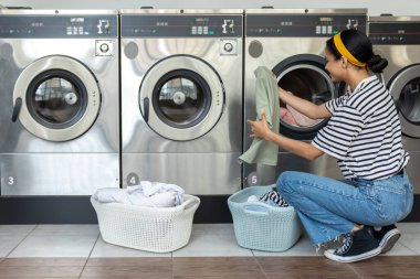 Çamaşırhanedeki esmer kadın, bozuk para kullanıldıktan sonra yeni yıkanmış giysileri katlıyor.