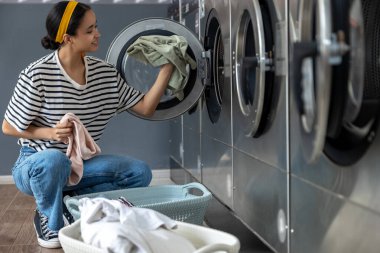 Çamaşırhanedeki yetişkin kadın müşteri kirli çamaşırları yıkamak için çamaşır makinesi kullanıyor.