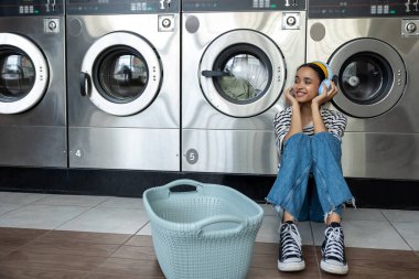 Günlük işleri sırasında müzik dinlerken endüstriyel çamaşır makinesi kullanan esmer kadın müşteri.