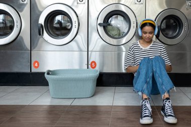 Çamaşırhanedeki kadın kulaklıklarıyla müzik dinlerken otomatik çamaşır makinesi kullanıyor.