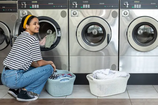 Çamaşırları yıkamak ve kurutmak için otomatik makine kullanan genç bir kadın.