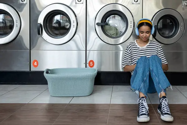 Çamaşırhanedeki kadın kulaklıklarıyla müzik dinlerken otomatik çamaşır makinesi kullanıyor.