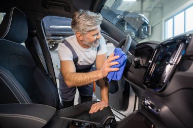 Otomobil salonundaki adam mikrofiber bez kullanarak araba panelini temizliyor ve temizliyor.