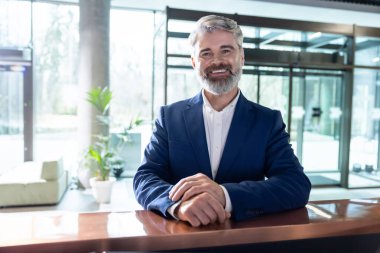 Modern ofis binasının lobisindeki resepsiyonist masasında poz veren sakallı girişimci.