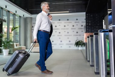 Havaalanı terminaline giderken yanında bavulla yürüyen sakallı bir adam.