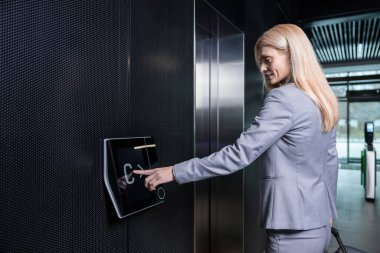 Asansörde. Zarif takım elbiseli sarışın kadın asansörü bekliyor.