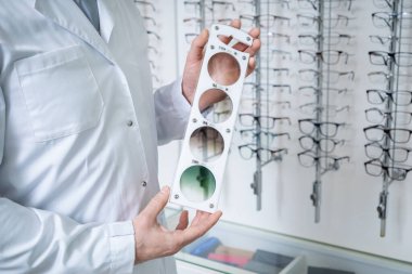 Lens renk ölçeği. Optik dükkanındaki erkek doktor ellerinde mercek rengi ölçeği tutuyor.