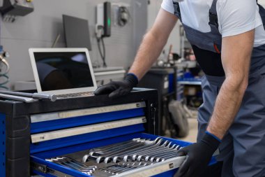 Üniformalı otomotiv teknisyeni tamir atölyesindeki araç motorunu kontrol etmek için dizüstü bilgisayar kullanıyor.