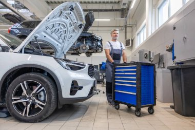 Otomobil atölyesinde üniformalı tamirci araç tamiri ve teşhisi için gerekli ekipmanla birlikte.