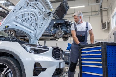 Otomobil atölyesinde üniformalı tamirci araç tamiri ve teşhisi için gerekli ekipmanla birlikte.