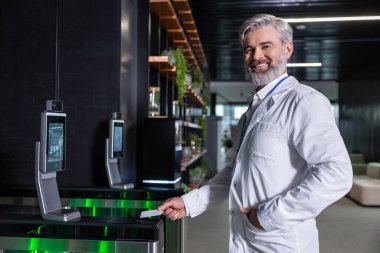 Klinik güvenlik kontrolü. Laboratuvar önlüklü erkek doktor kliniğe giriş kartını kullanarak giriyor.