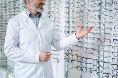 Optik dükkan. Sakallı erkek göz doktoru bir optik dükkanında yeni gözlük gösteriyor.
