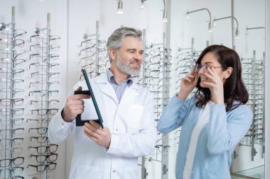 Optik mağazasında gözlük takan kadın müşteri. Doktor da görme yeteneğinin gelişmesine yardımcı oluyor.