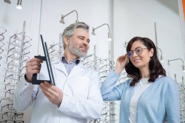 Optik mağazasında gözlük takan kadın müşteri. Doktor da görme yeteneğinin gelişmesine yardımcı oluyor.
