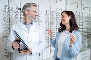 Optik mağazada optik rehber seçeneğiyle gözlük seçen neşeli kadın müşteri