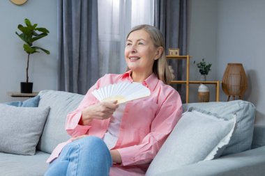 Menopoz belirtileri. Elinde yelpaze olan pembe gömlekli orta yaşlı bir kadın.