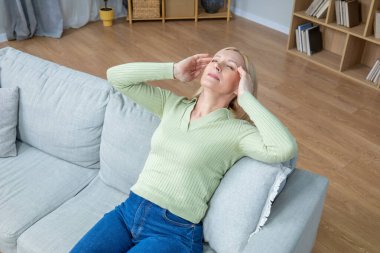 Baş ağrısı. Kanepede oturan ve baş ağrısı çeken sarışın bir kadının en iyi görüntüsü.