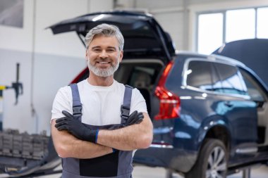 Garajda çalışan üniformalı bir adam otomobili kontrol ediyor ve tamir ediyor.