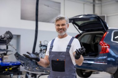 Garajda çalışan üniformalı bir adam otomobili kontrol ediyor ve tamir ediyor.