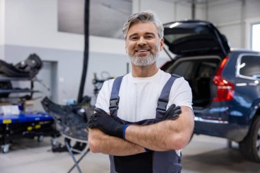 Atölyedeki gri saçlı tamirci tamir işinde otomobil parçalarını kontrol edip tamir ediyor.