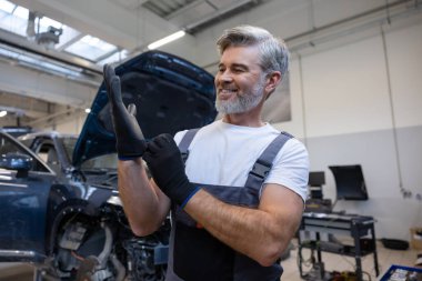 Atölyedeki gri saçlı tamirci tamir işinde otomobil parçalarını kontrol edip tamir ediyor.