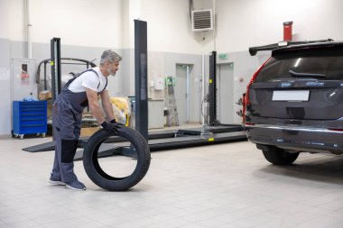 Otomotiv teknisyeni garajda tekeri kontrol ediyor ve garajda araç güvenliğini sağlıyor.
