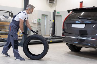 Otomotiv teknisyeni garajda tekeri kontrol ediyor ve garajda araç güvenliğini sağlıyor.