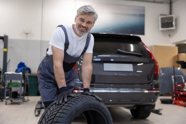 Otomotiv teknisyeni garajda tekeri kontrol ediyor ve garajda araç güvenliğini sağlıyor.